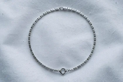 Gourmette en argent pour bébé posée sur tissu blanc, vue de dessus, avec maillons gravés et fermoir en forme de cœur