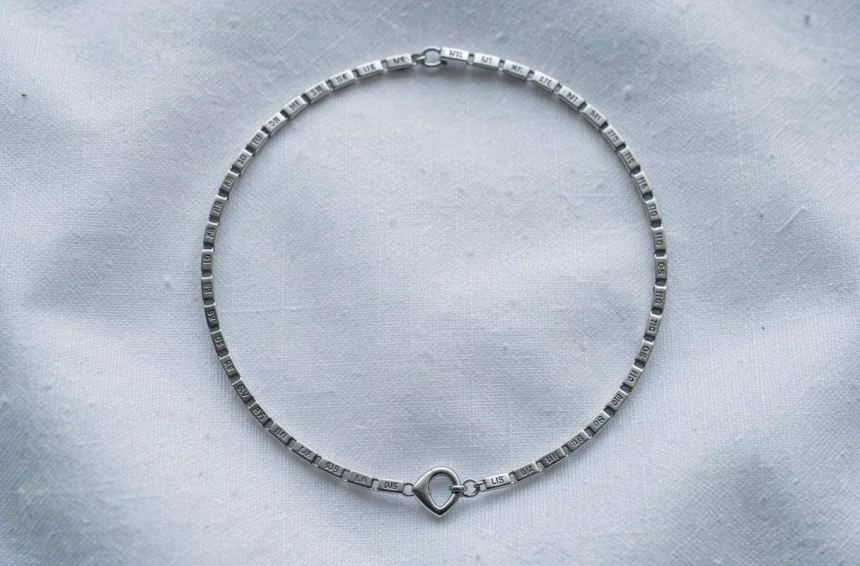 Gourmette en argent pour bébé posée sur tissu blanc, vue de dessus, avec maillons gravés et fermoir en forme de cœur